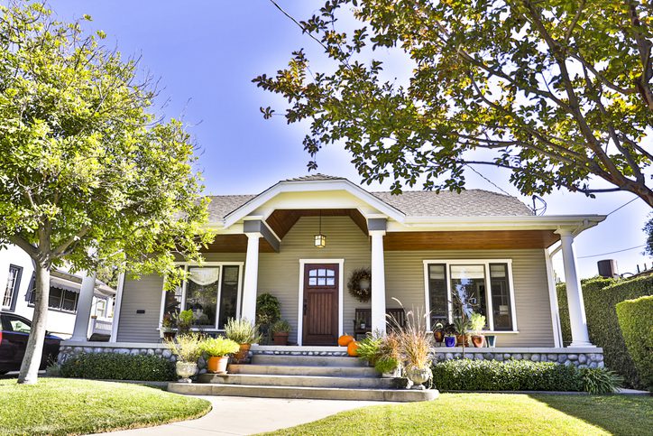 A charming beige house with a welcoming front porch and greenery.